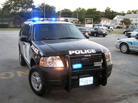 1991 Ford Crown Victoria - A black police SUV with its light bar illuminated is parked next to another police vehicle.