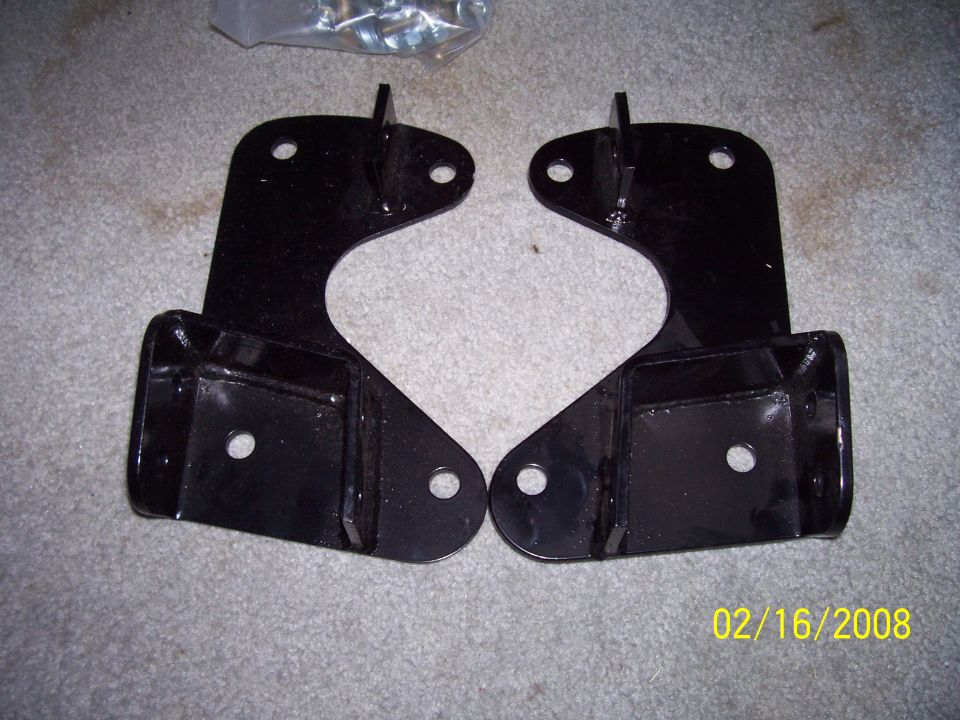 Pair of black metal lift kit brackets on a carpeted surface