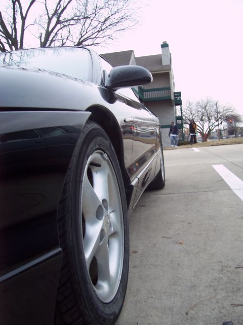 1993 Ford Probe - A black coupe is parked on pavement with a building and trees visible in the distance.