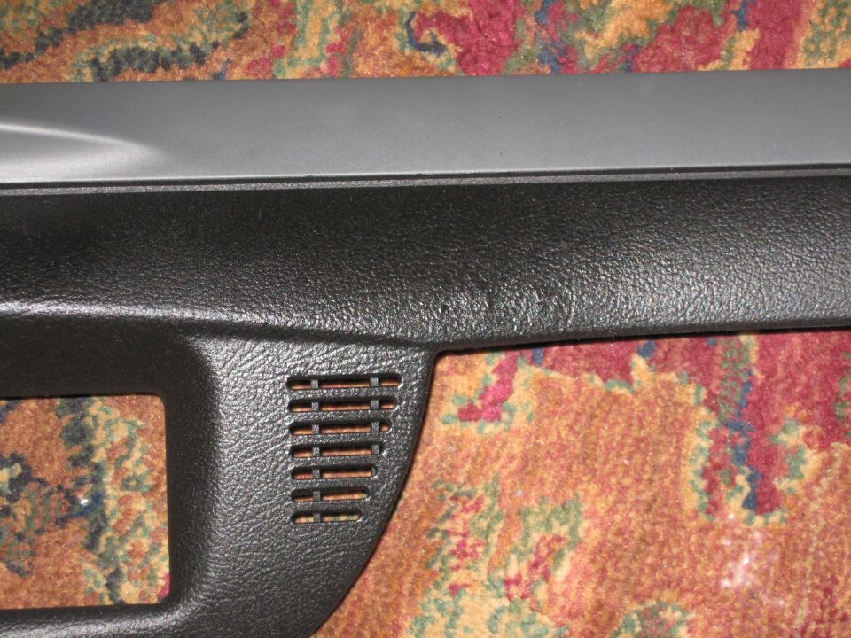 Close-up of a black plastic dashboard trim piece with a vent, resting on a patterned carpet