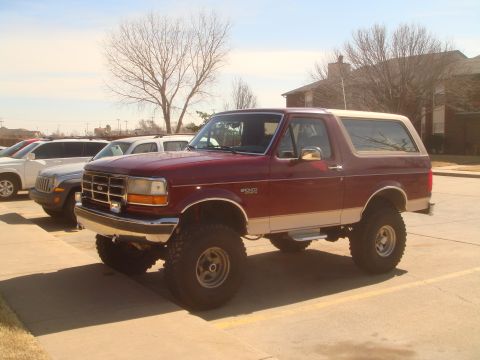 1992 Ford Bronco - A maroon and tan Ford Bronco is parked in a lot with other vehicles visible in the background.