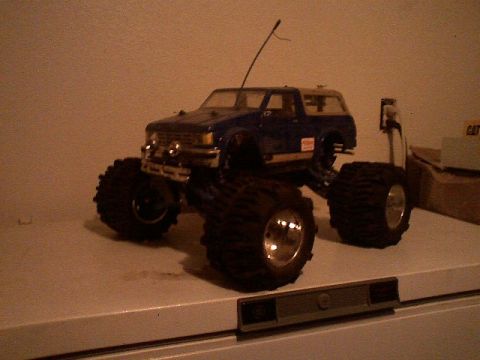 1991 Ford Bronco - A blue remote control monster truck sits on a shelf, its large tires dominating the frame.