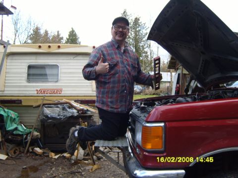 1989 Ford Bronco - Man kneels on the bumper of a red truck with its hood open, holding a level.