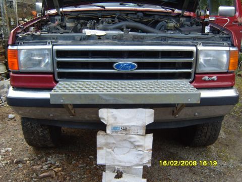 1989 Ford Bronco - Front view of a red Ford truck with its hood up, revealing the engine compartment and grille. A step is mounted on the bumper.