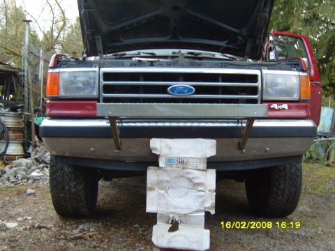 1989 Ford Bronco - The front of a red 1989 Ford Bronco is visible with its hood open, revealing the grille and headlights.