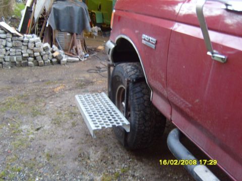 1989 Ford Bronco - The side of a red 1989 Ford Bronco is visible, a metal step and large tire. The vehicle appears to be parked outdoors.