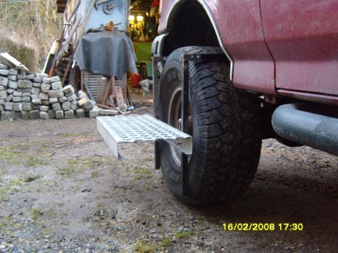 1989 Ford Bronco - Rear detail of a maroon Ford truck showing a spare mud-terrain tire mounted on a custom carrier with a galvanized diamond-plate step below…