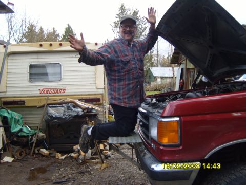 1989 Ford Bronco - A man in a plaid flannel shirt and cap throws his arms up beside a red Ford truck with its hood raised in a muddy rural yard, dated 16/02/2…