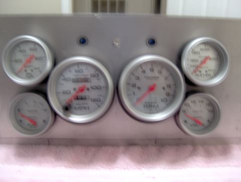 1978 Ford Bronco - A set of aftermarket dashboard gauges, including a speedometer, tachometer, water temperature, and voltage meter, are mounted on a silver p…