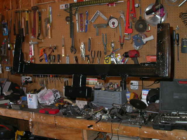 Painted vehicle frame member on a workbench with pegboard tools