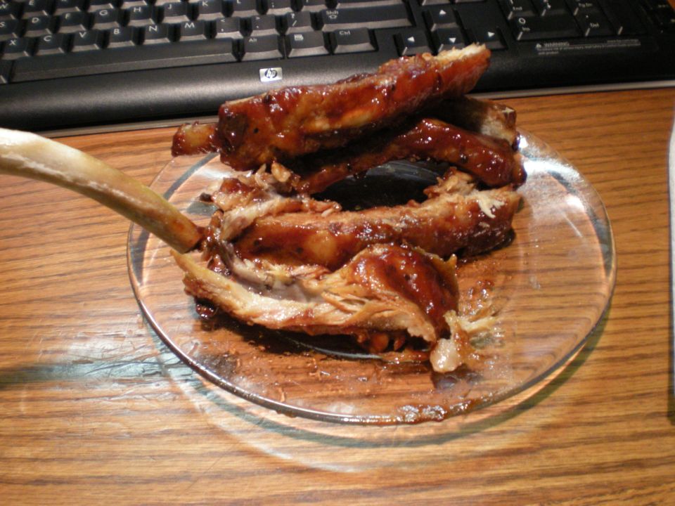 Plate of BBQ ribs on a wooden desk in front of a computer keyboard