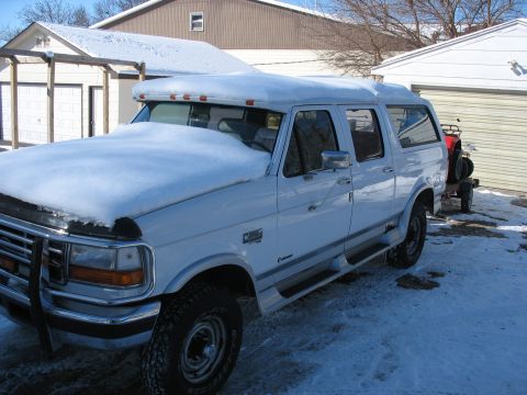 1995 Ford C-350 (Centurion Conversions) - A white extended cab pickup truck with a camper shell is parked in a snowy driveway.