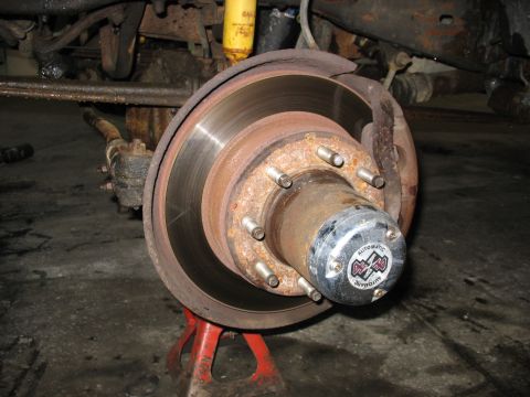 1995 Ford C-350 (Centurion Conversions) - Close-up of a vehicle's front wheel hub and brake assembly, supported by a red jack stand.