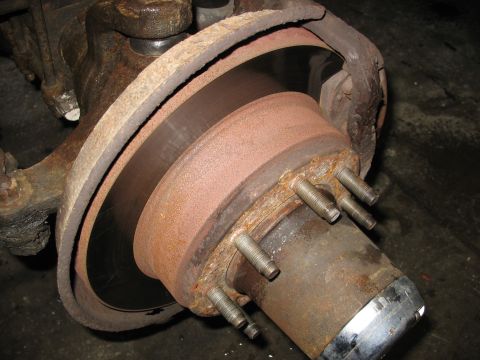 1995 Ford C-350 (Centurion Conversions) - Close-up view of a rusty front axle hub and brake rotor, likely needing replacement.