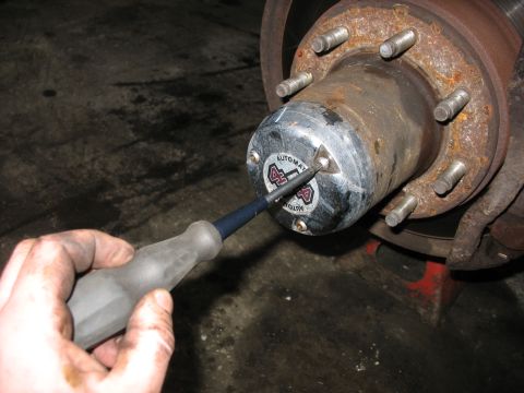 1995 Ford C-350 (Centurion Conversions) - A screwdriver is used to remove the cap from an automatic locking 4x4 hub assembly on a vehicle's front axle.