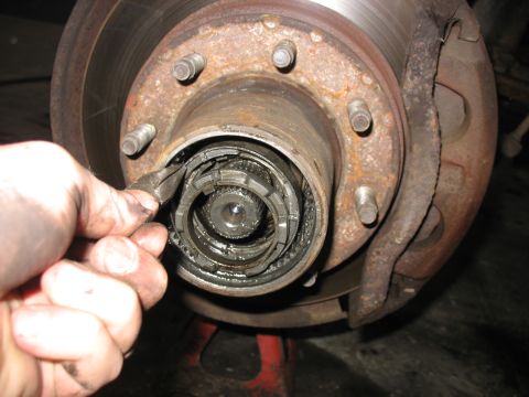 1995 Ford C-350 (Centurion Conversions) - A hand works on the front wheel hub assembly of a vehicle, showing internal gears and a rusty brake caliper.