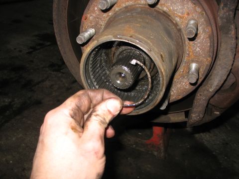 1995 Ford C-350 (Centurion Conversions) - Close-up of a vehicle's front wheel hub assembly with a C-clip being held by a greasy hand.