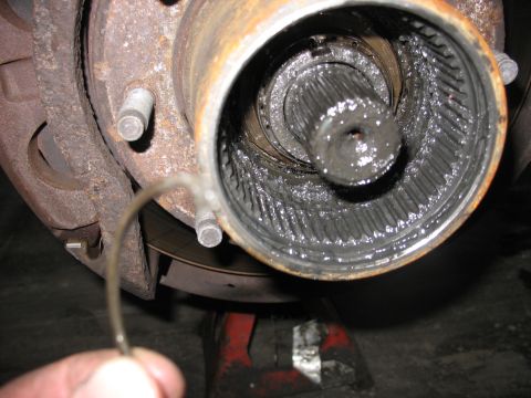 1995 Ford C-350 (Centurion Conversions) - A mechanic holds a bent metal clip near a disassembled front axle hub, revealing a splined shaft coated in old grease.
