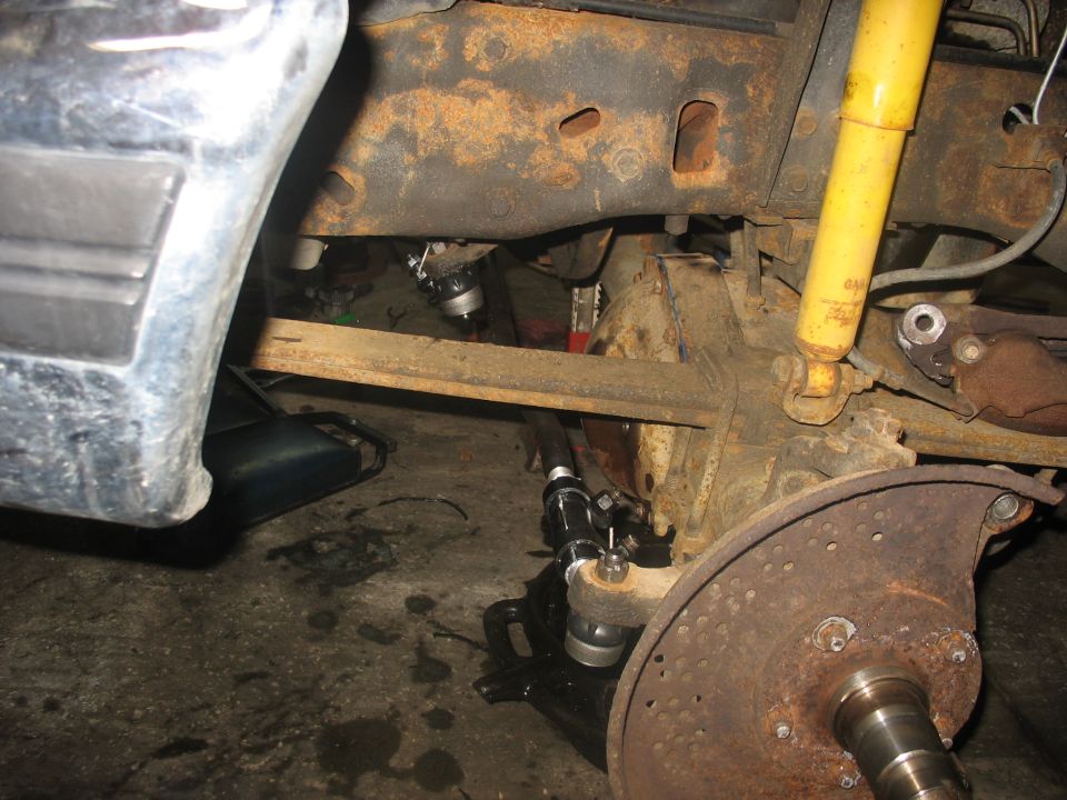 Close-up of a rusty front axle assembly with a yellow shock absorber and brake rotor