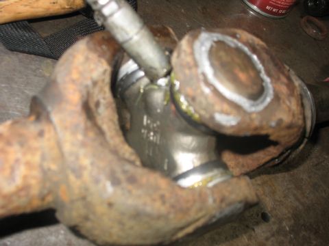 1995 Ford C-350 (Centurion Conversions) - Close-up of a rusty front axle U-joint, showing part numbers and signs of repair.