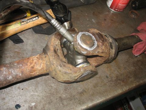 1995 Ford C-350 (Centurion Conversions) - Servicing a driveshaft universal joint with a grease gun and hammer on a workbench.
