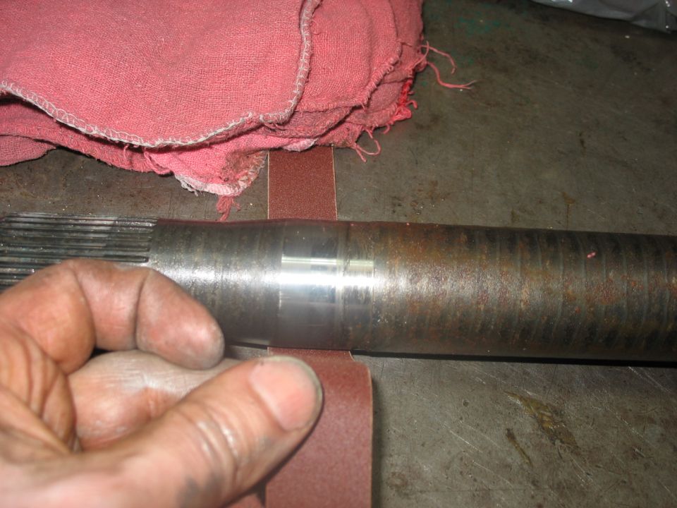 Hand sanding an axle shaft with splines on one end and a smooth section with a groove on the other