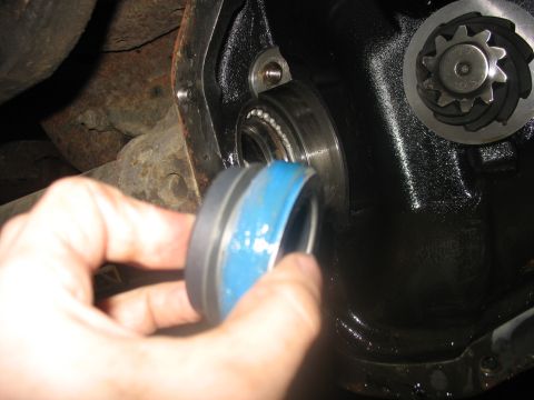 1995 Ford C-350 (Centurion Conversions) - Close-up of a vehicle differential housing with a hand holding a seal, preparing for repair.
