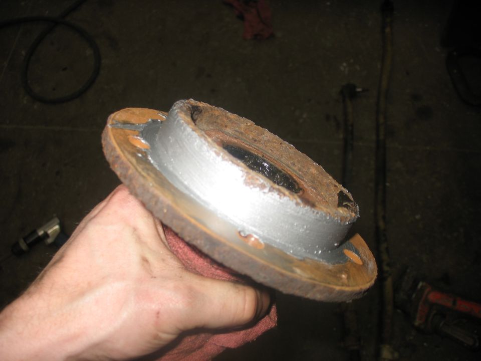 Hand holding a rusty wheel hub with a brake rotor attached. Some parts have been cleaned and painted silver