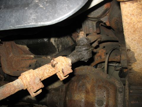 1995 Ford C-350 (Centurion Conversions) - Close-up view of the steering linkage and front axle differential, showing significant rust and grease.