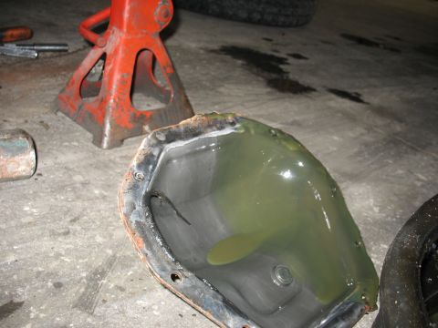 1995 Ford C-350 (Centurion Conversions) - A differential cover filled with old, murky fluid sits on a concrete floor next to jack stands, indicating a front axle rebuild.