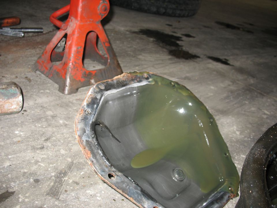 Differential cover with old fluid and a crack, on a concrete floor with jack stands