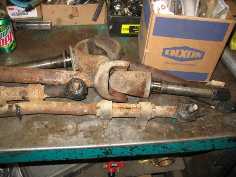 1995 Ford C-350 (Centurion Conversions) - Several heavily rusted automotive parts, including a driveshaft and steering components, are laid out on a metal surface.