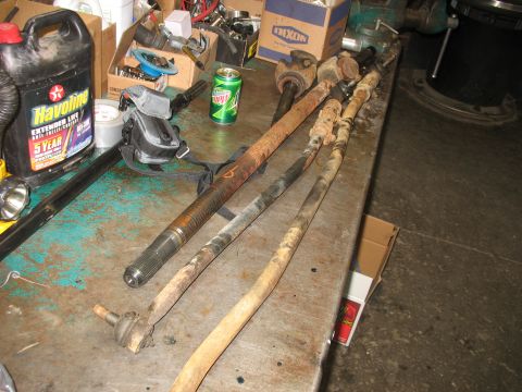1995 Ford C-350 (Centurion Conversions) - Various front axle components, including tie rods and driveshaft parts, are laid out on a workbench, likely for a rebuild or repair.
