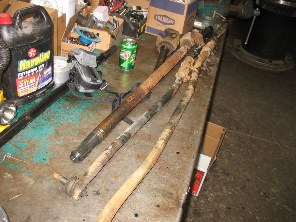 Front axle components including tie rods and driveshaft parts on a workbench