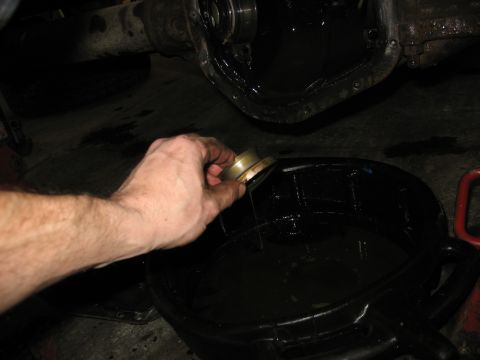 1995 Ford C-350 (Centurion Conversions) - Draining fluid from a vehicle's front axle differential into a black oil pan during a rebuild.