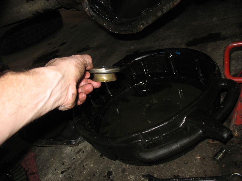 Hand holding a differential cover bolt over a black oil drain pan filled with used fluid