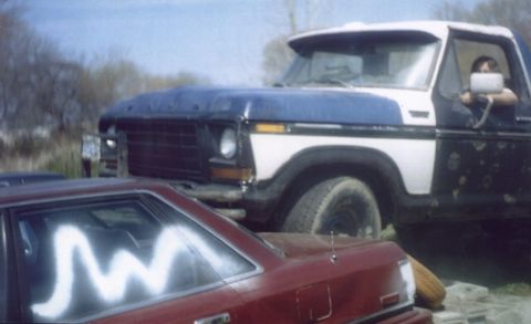 1978 Ford Bronco - A blue and white Ford truck is parked closely behind a red car, with a person visible in the driver's seat.