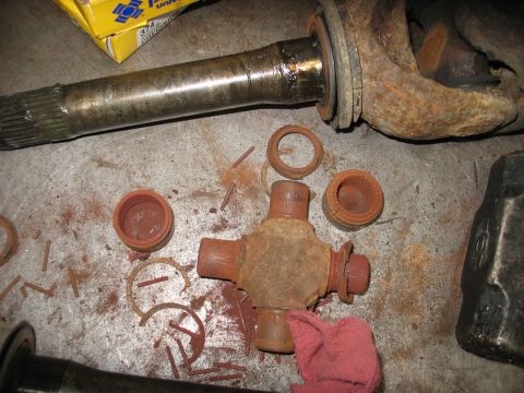 1995 Ford C-350 (Centurion Conversions) - Disassembled front axle components, including a U-joint and axle shaft, lie on a metal surface next to a red cloth and a sledgehammer.
