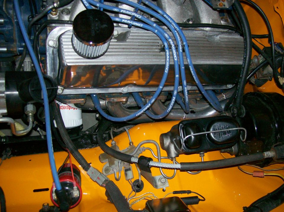 Engine bay with chrome valve covers, blue spark plug wires, and yellow paint