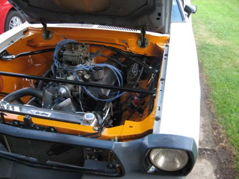 1978 Ford Mustang II - The engine bay of a 1978 Ford Mustang II is open, revealing a V8 engine with orange painted inner fenders.