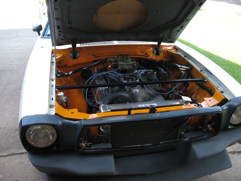 Engine bay of white coupe with orange-painted core support, carbureted V8 and Griffin aluminum radiator