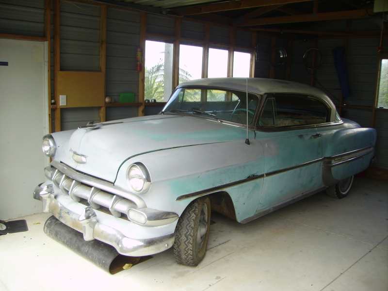 old car with primer and blue paint, parked inside a shed