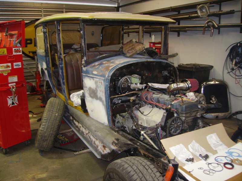 Vintage car body with engine exposed, undergoing restoration in a garage. Tools and parts are visible