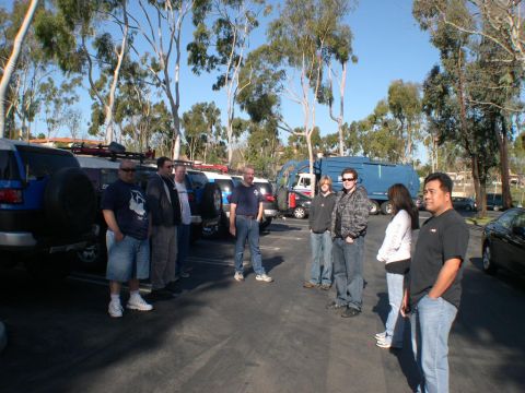 2007 Toyota FJ Cruiser - A group of people gathered around several Toyota FJ Cruisers in a parking lot on a sunny day.