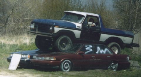 1978 Ford Bronco - A blue and white 1978 Ford Bronco is stacked on top of two sedans in an outdoor setting.