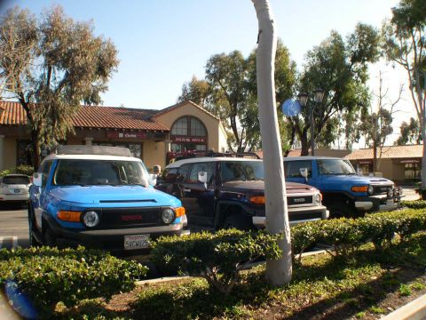 2007 Toyota FJ Cruiser - Three Toyota FJ Cruisers are parked together in a lot, with a building and trees in the background.
