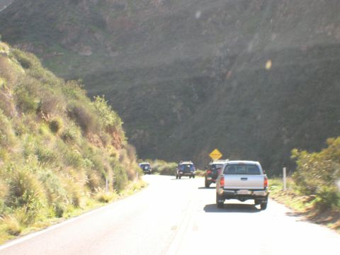 2007 Toyota FJ Cruiser - A convoy of vehicles travels along a scenic, winding road with a steep, vegetated hillside.
