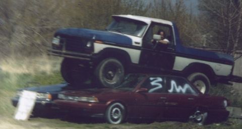 1978 Ford Bronco - A blue and white pickup truck is shown crushing a red sedan, which has white graffiti on its window.