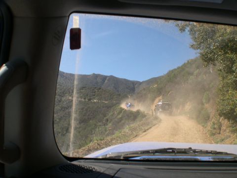 2007 Toyota FJ Cruiser - Two SUVs navigate a dusty mountain road, kicking up clouds of dirt under a clear blue sky.