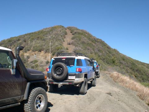 2007 Toyota FJ Cruiser - Several FJ Cruisers drive up a dusty mountain trail under a clear blue sky.